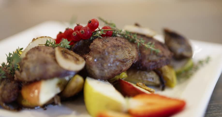 A plate of food containing grilled steak potatoes apple and cut strawberry is topped with an appealing garnish