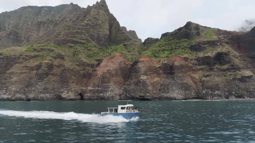 A blue boat sailing on the ocean near a cliff