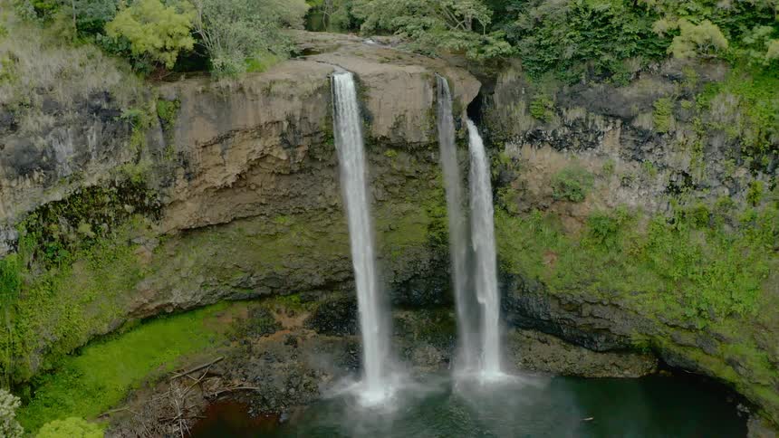 Three waterfalls splash into a ravine below a cliff
