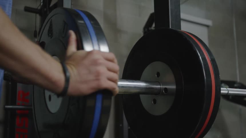 A man adds weights to a long barbell in a gym