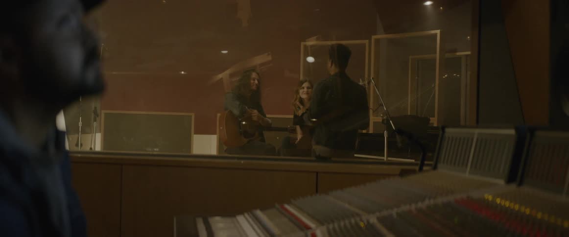 Musicians talk in sound booth while the technician studies the soundboard