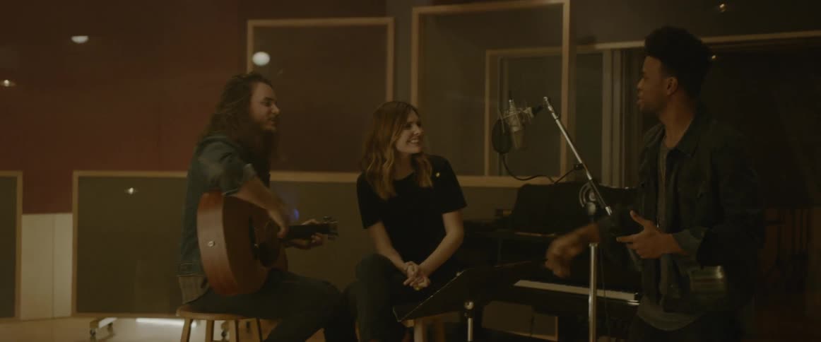 Three people talk in a studio and one plays a guitar