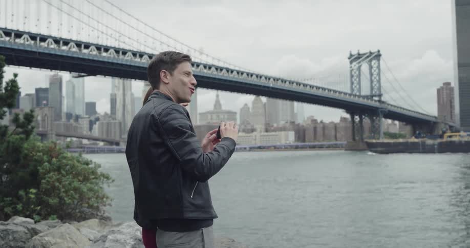 A white man and woman stand together posing for pictures near the brooklyn bridge