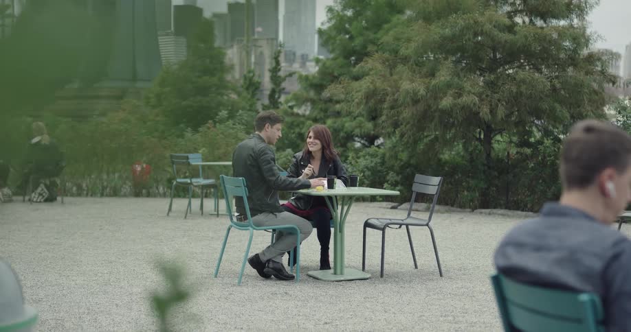 A man and woman in leather jackets eating at an outdoor table in a park
