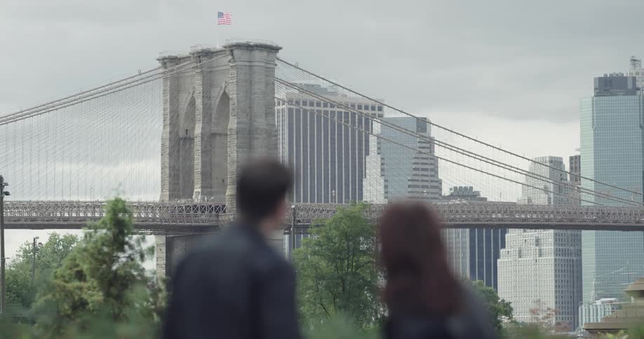A man and woman in leather jackets talking while looking at a city bridge in the distance