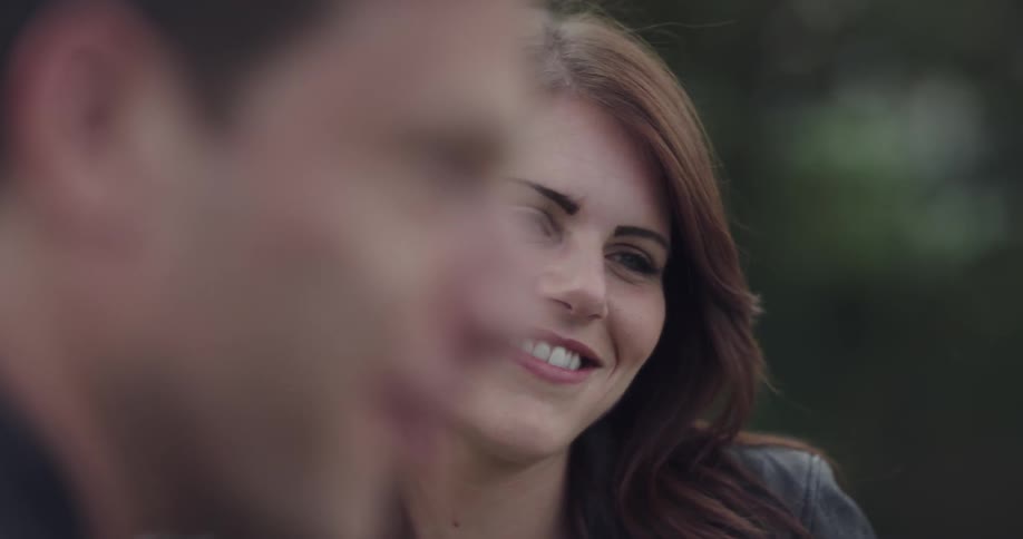 Woman wearing black leather jacket talks to man and smiles during daylight