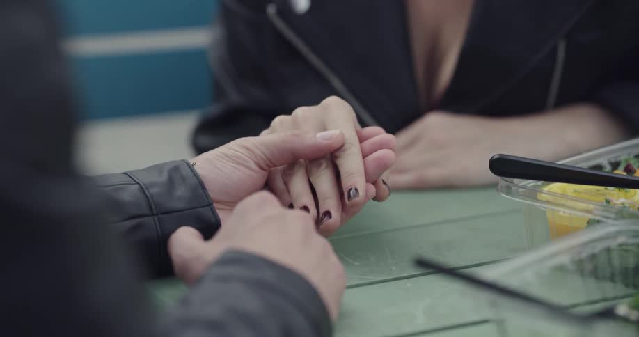 Woman and man sitting at the table hold hands and laugh in the public park during daylight