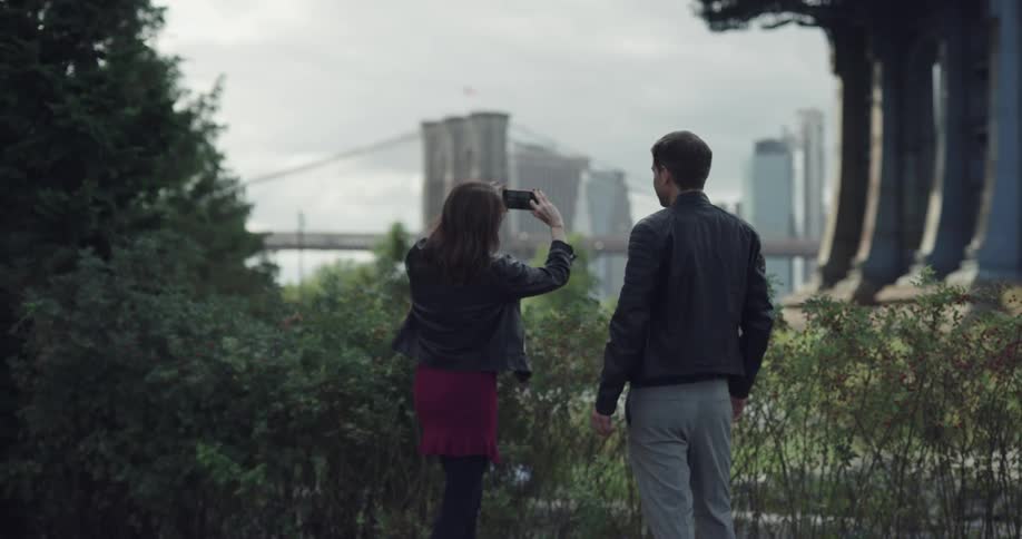 Couple taking picture of a brooklyn bridge with phone on the public park