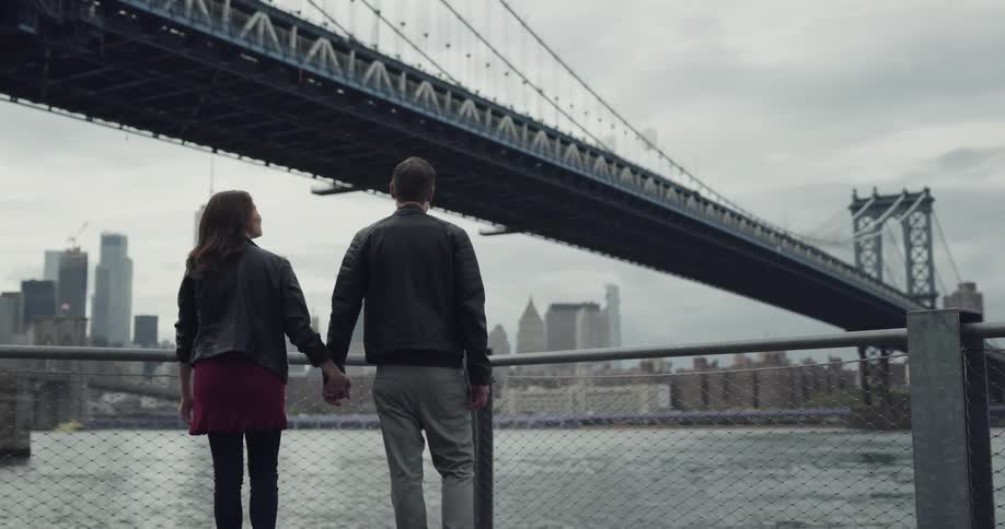 Couple holding hands walking towards the bay to admire a bridge in the city