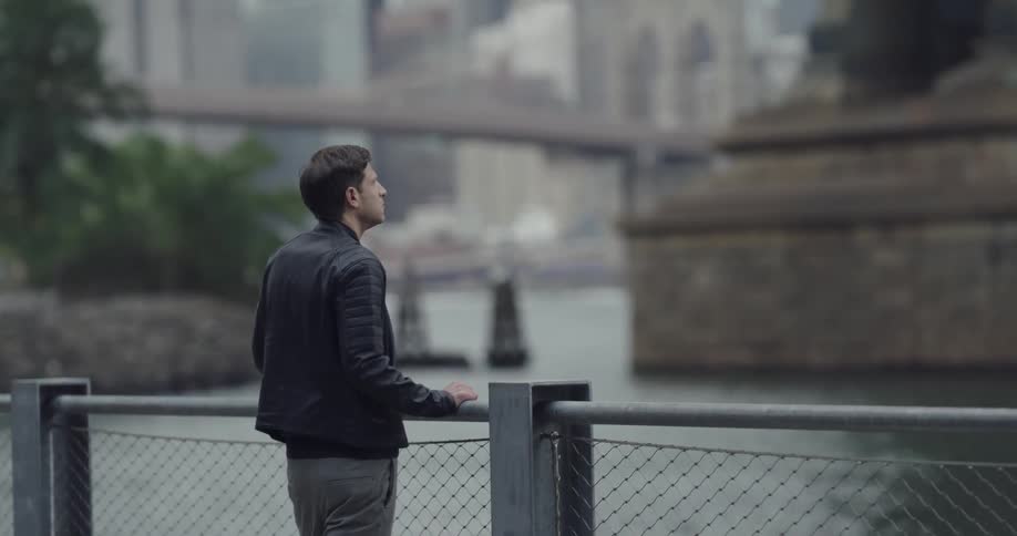 Man stands at waterfront looking at bridge tower base near downtown