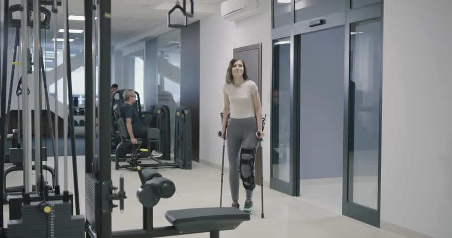 A female with a leg brace and crutches walking into a gym