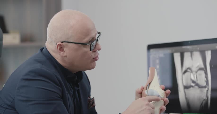 A man holds a model of a knee and explains it to another man