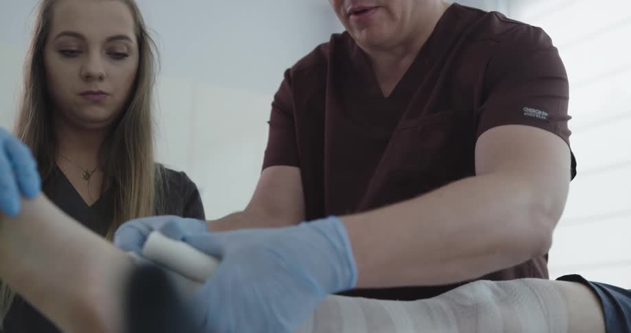 A nurse hands a doctor some gauze and he wraps a womans leg