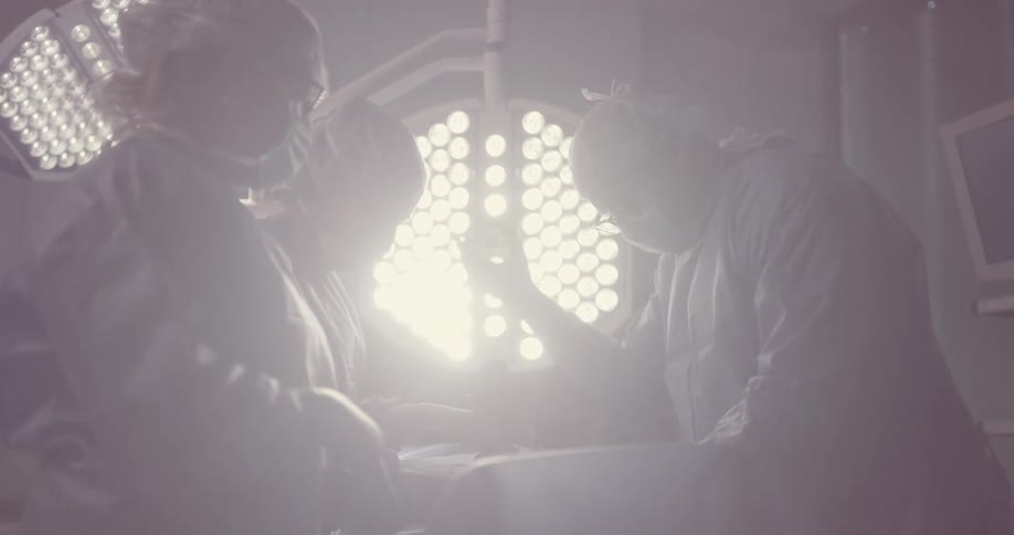 A surgeon pulls a bright light closer and over the operating table