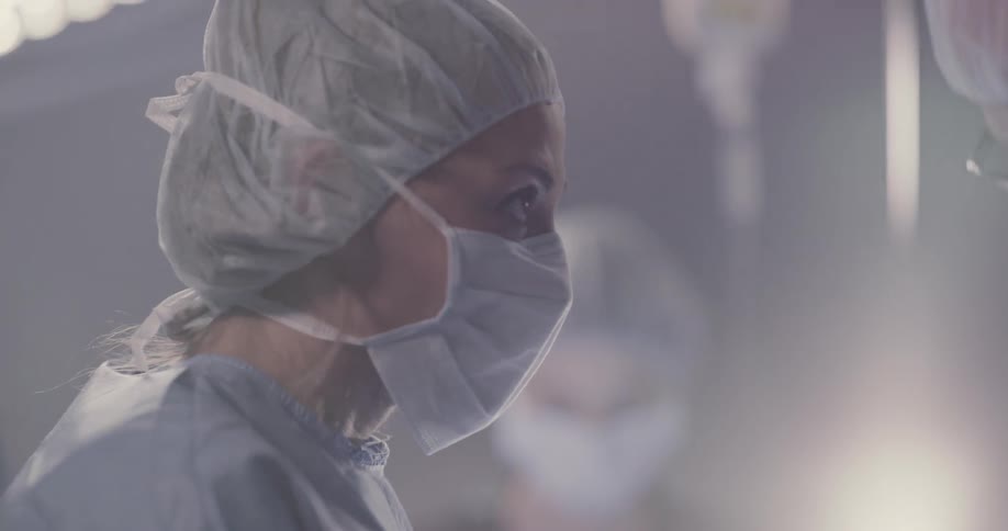 A team of surgeons all wearing face masks concentrates and focuses on their patient below them