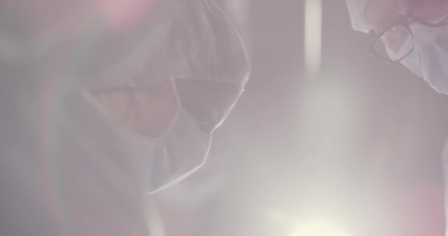 A doctor and nurse bend over a operating table
