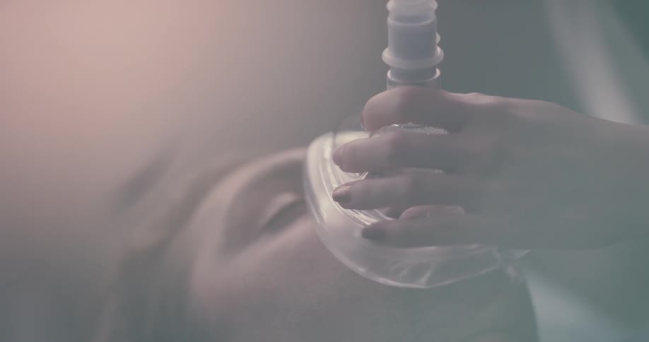A man lays on a table with his eyes closed and someone places an oxygen mask on his face