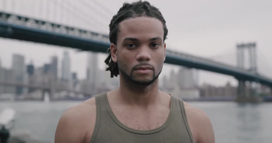 Man stands outdoors with river bridge and downtown in background