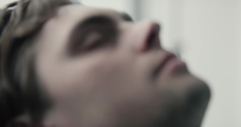 A sleeping young man with his head on an elevated blue pillow in a room with white walls