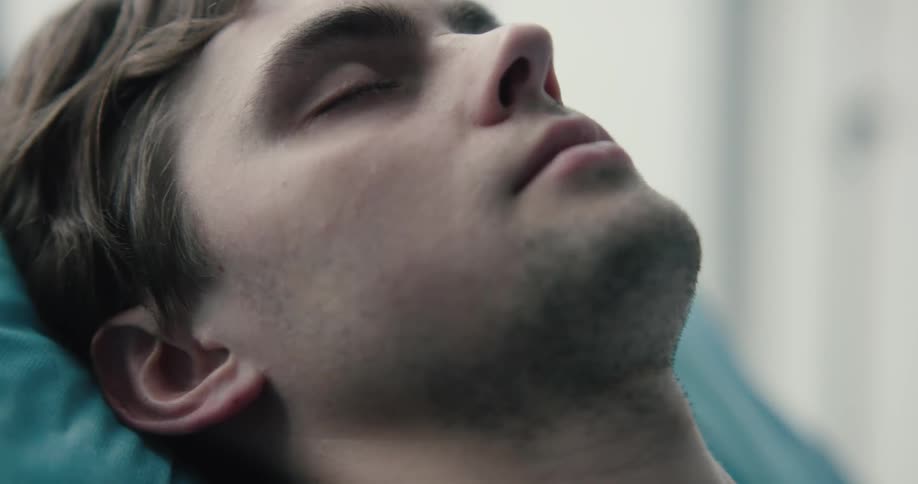 An adult male is seen sleeping while partially inclined in a hospital bed in a bright room