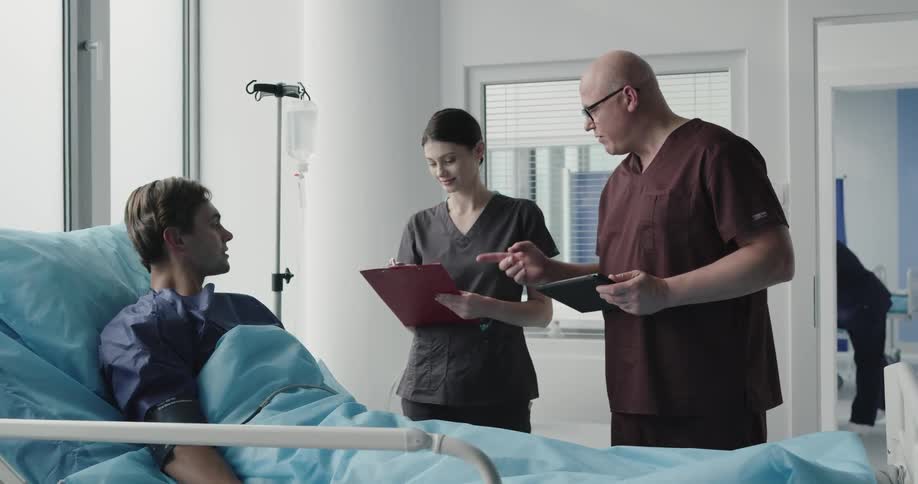 A man and woman talk to a patient in a hospital room
