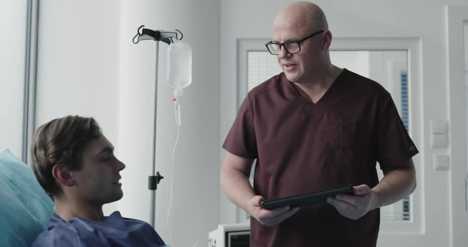 A bald male nurse with a tablet talking to a patient