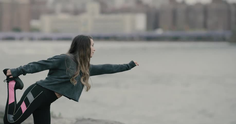 Woman warms up before running by the river side in new york city during daylight