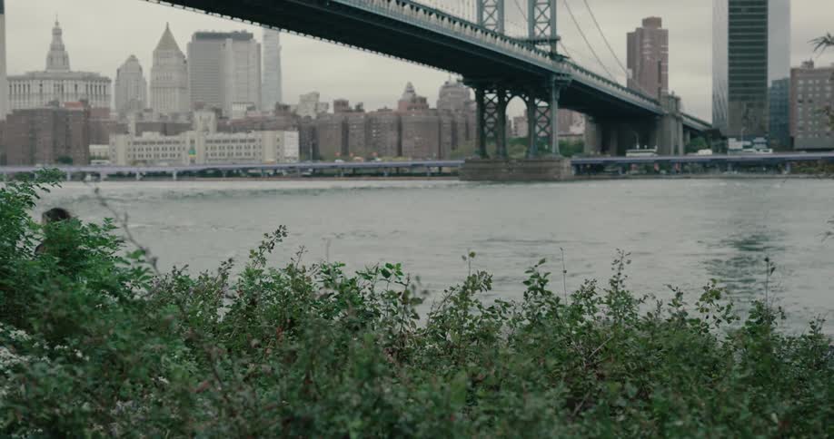 Woman runs along on the promenade next to the river across brooklyn bridge and new york city on a cloudy day