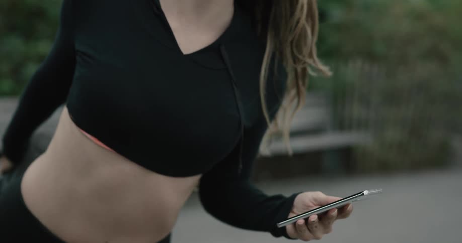 A woman puts in her earphones while stretching and holding her phone