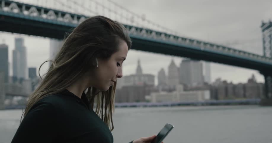 A woman stretches in front of the water and looks at her cell phone