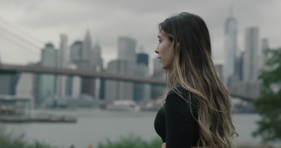 Woman uses smartphone and looks at the bridge and the city on a cloudy day