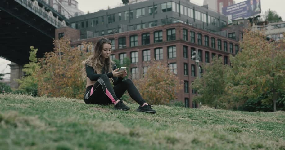 A young woman sits on a hill and looks at her cell phone