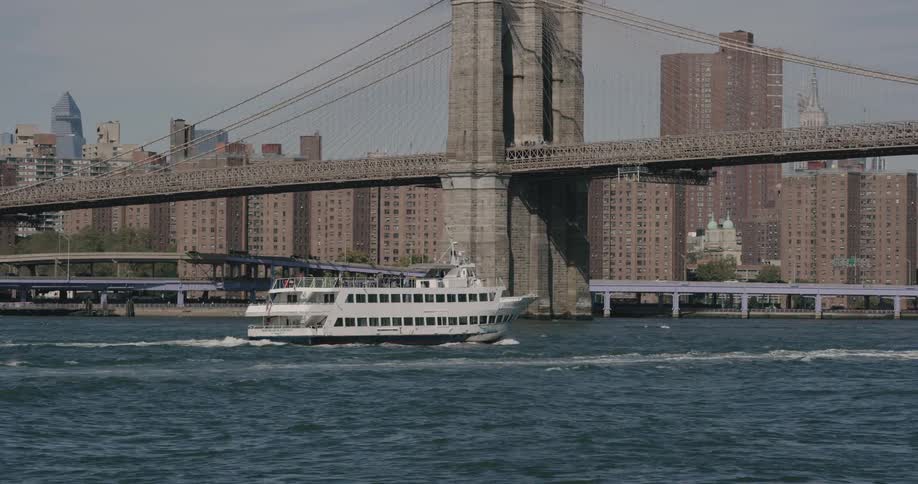 A ferry sailing on the river under brooklyn bridge
