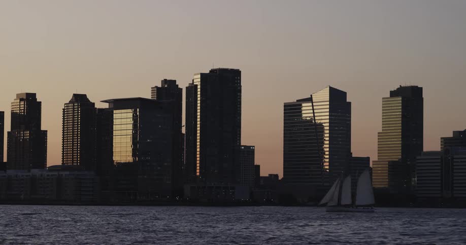 A boat sails through the water in front of a city at dusk