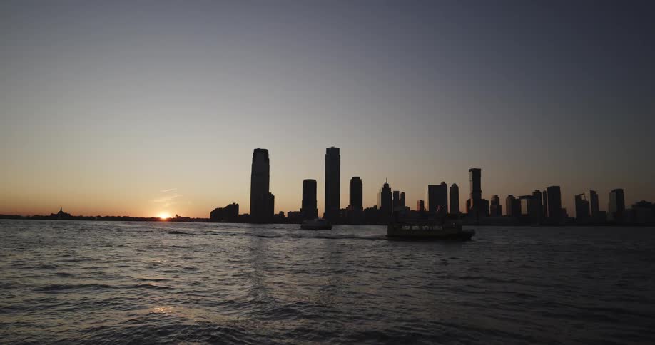 Skyline of the city with tall buildings and ferries float along the sea at sunset