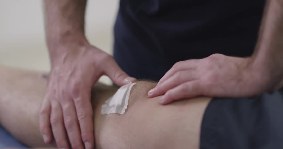 A massage therapist kneads the knee of a man sitting on a table