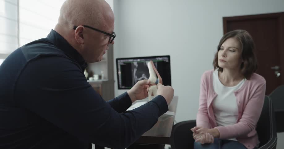 A doctor uses a knee joint model while meeting with a female patient