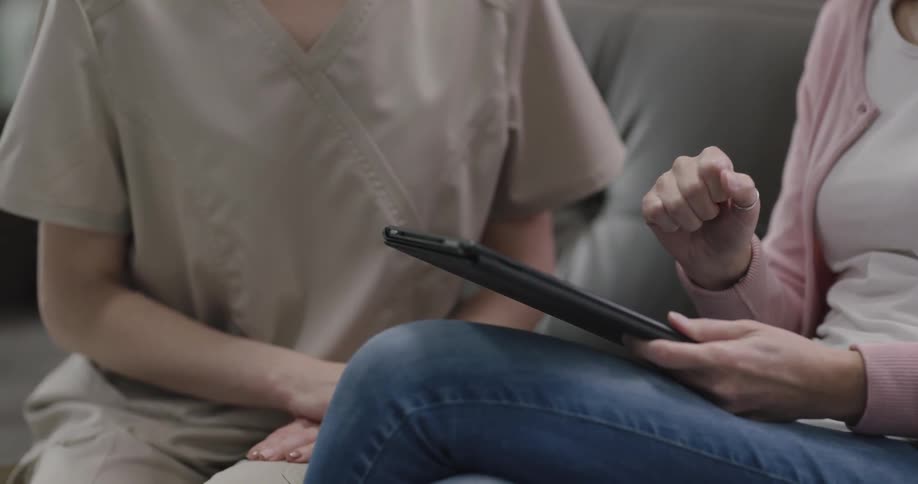 Two women sit together and use a tablet