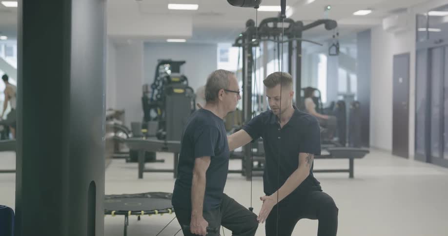 A gym instructor helping on man works out
