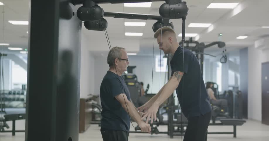 An elderly man doing resistance exercise with the help of a personal trainer