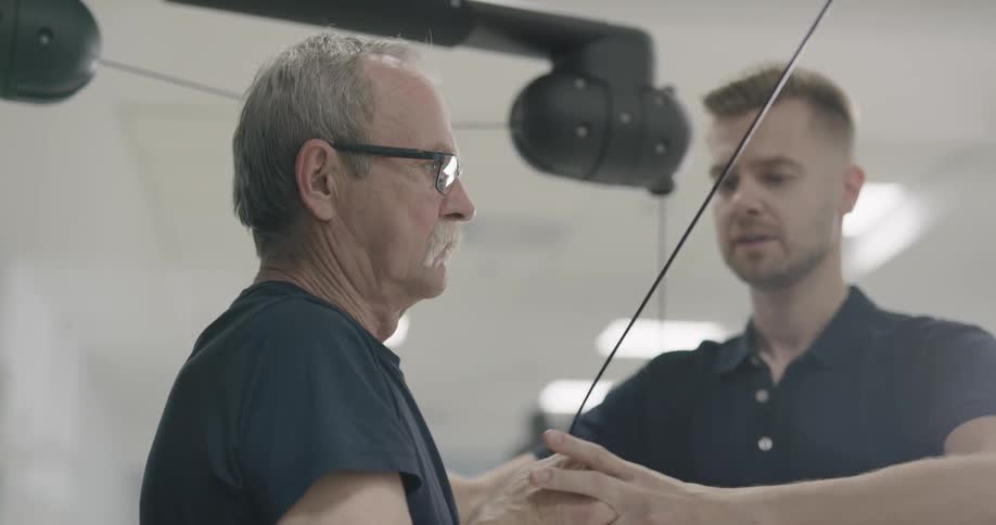 A trainer is helping a man exercise in a gym