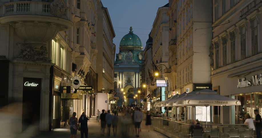 A busy shopping area in a downtown area near a cathedral is filled with people coming and going under the night sky