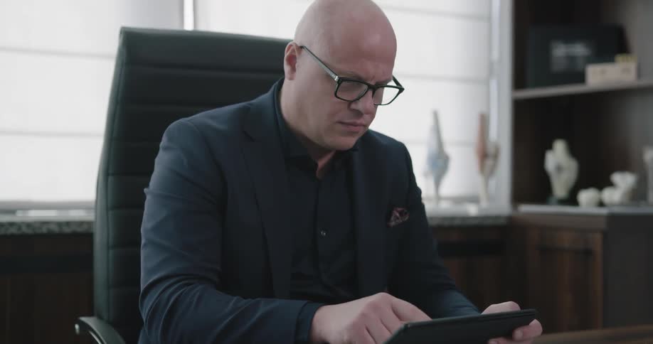 A man sits at his desk and uses his tablet