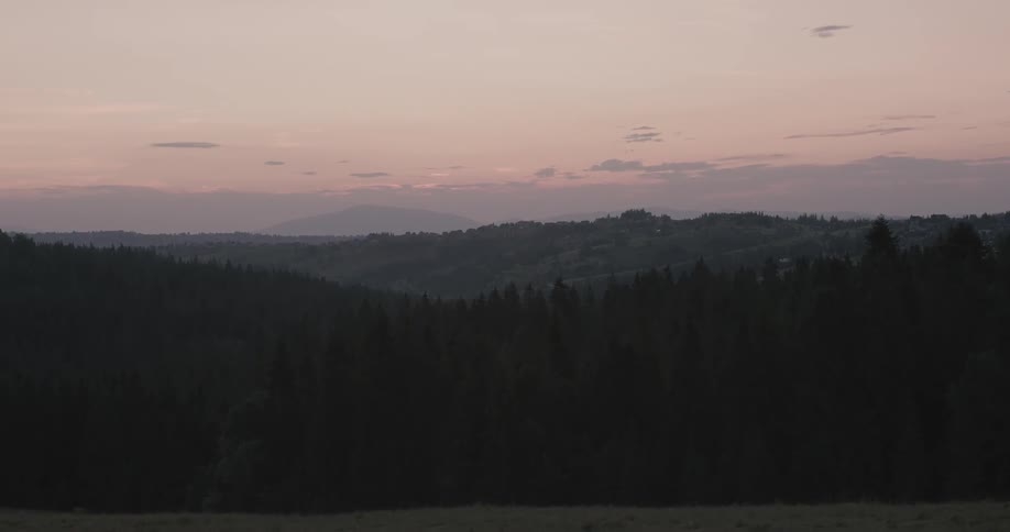 Trees are outlined on a hilly landscape at sunset