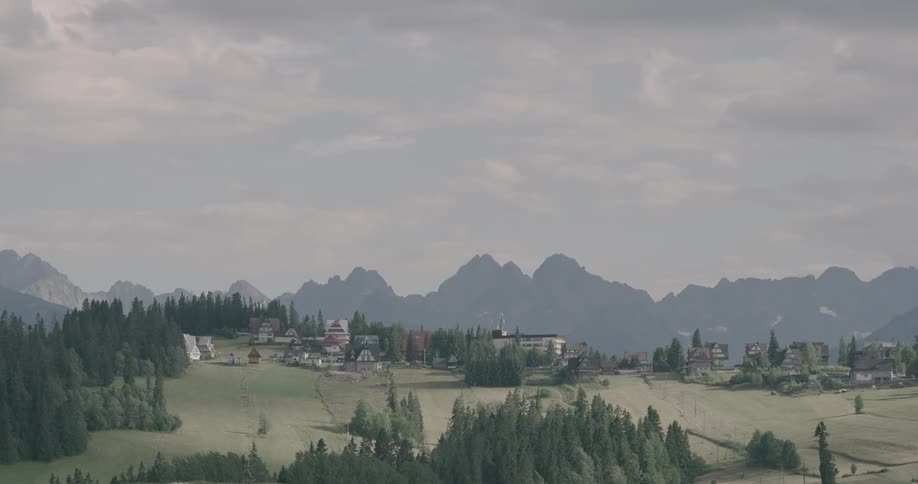 A green village with many houses sits in a valley with mountains all around it under a cloudy sky
