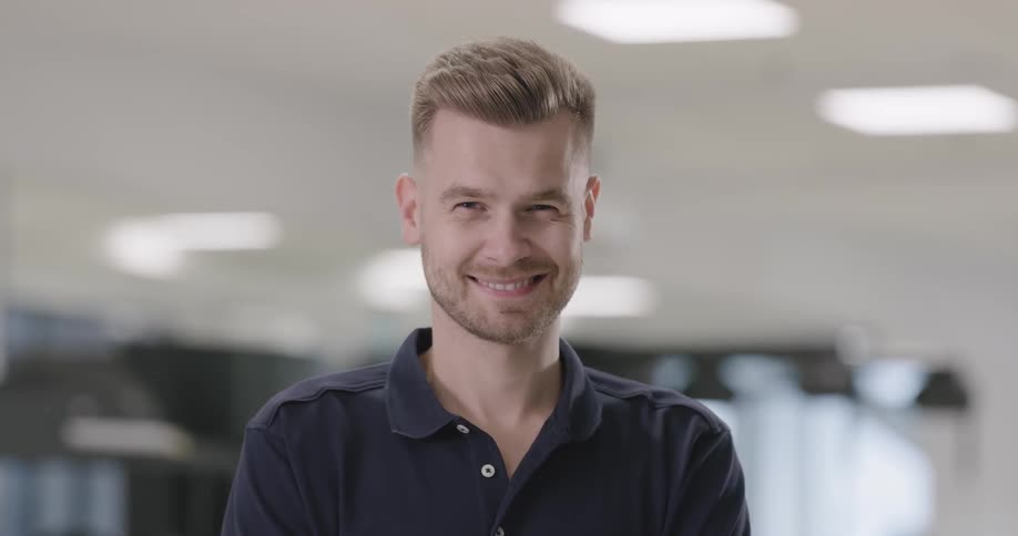 Blonde man wearing dark blue polo shirt looks at the camera and smiles in the hospital