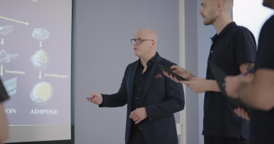 Several people watch a bald man give a presentation on a screen