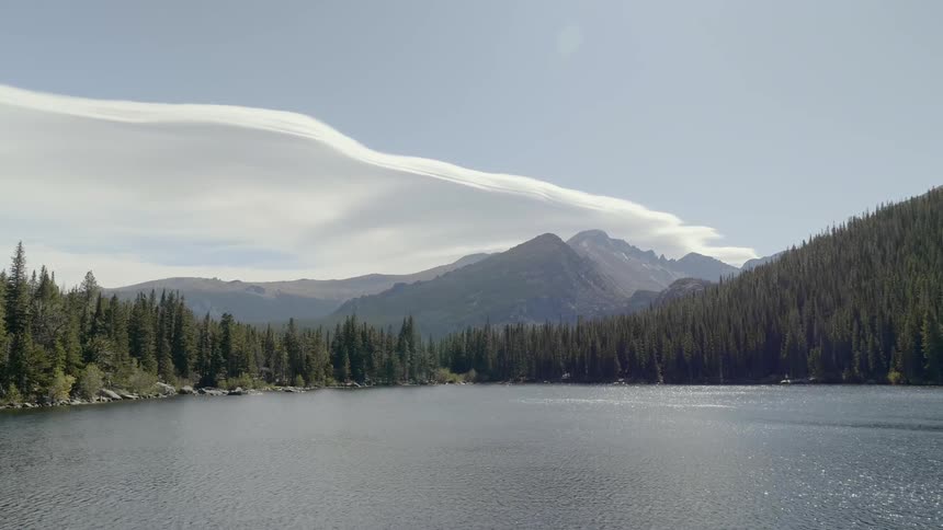 Cloud front rolls in over mountain range behind forest and lake