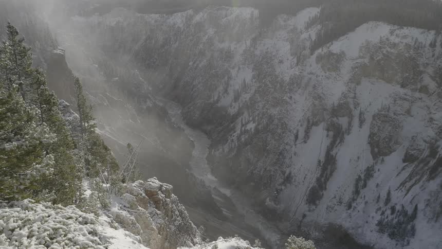 Fog covers river flowing between snow covered mountains and forest
