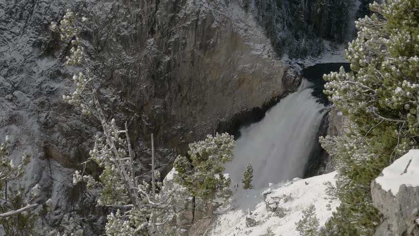 Waterfalls cascades down between snow covered slopes